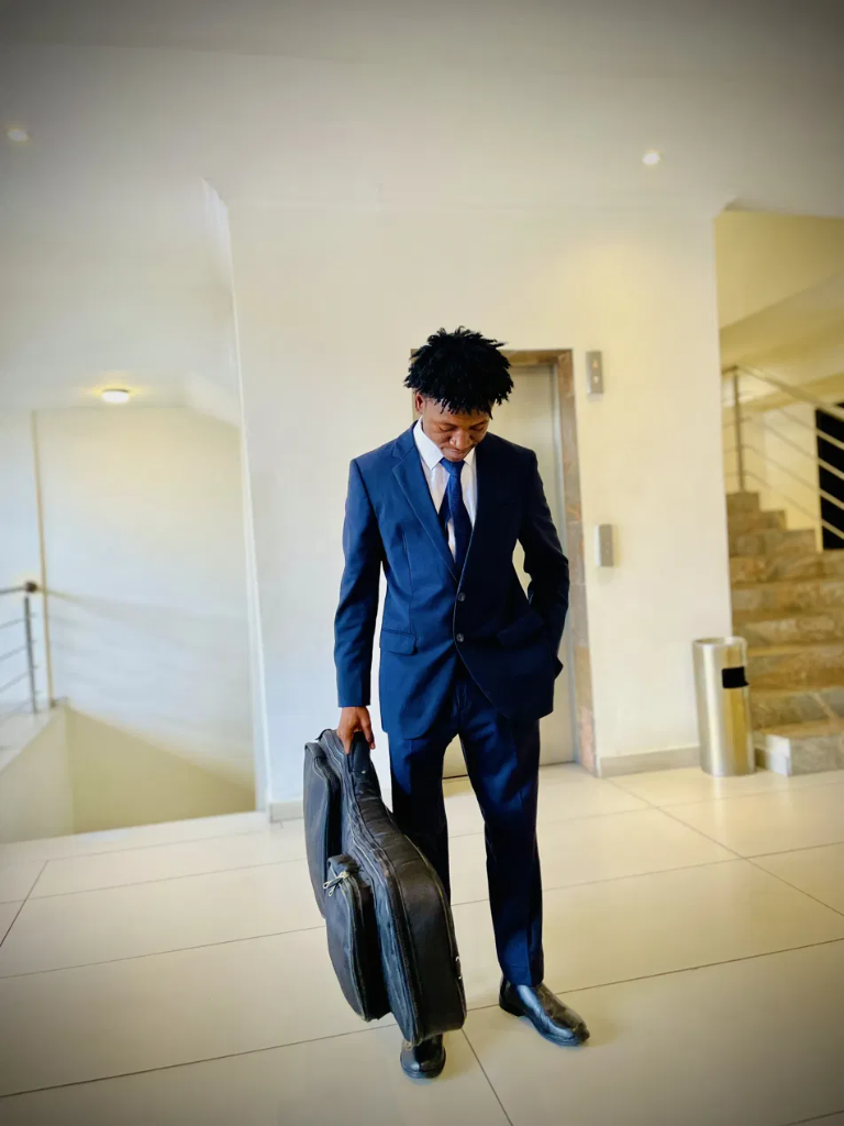 Denbasz Wurld in a navy suit holding his bass case